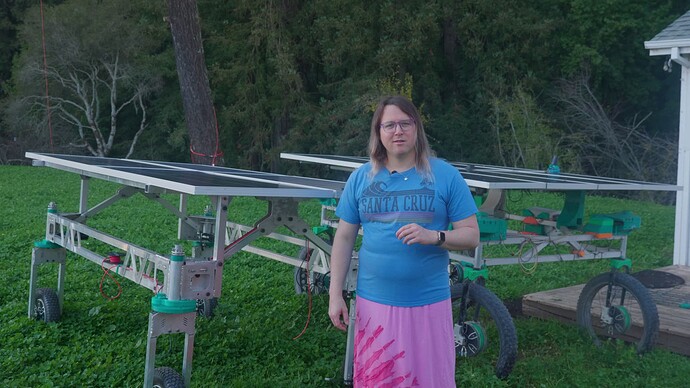 Taylor standing in front of two prototype robotic vehicles, the original prototype and a new one.